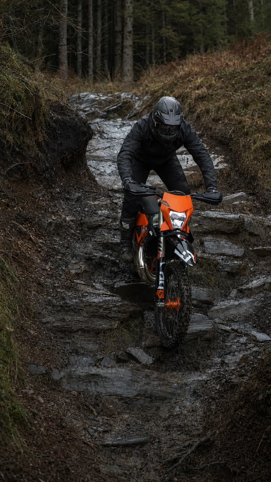 An enduro rider approaching down a rocky woodland trail